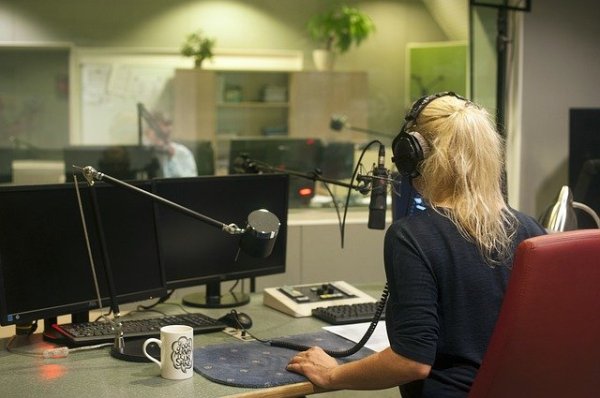 Une jeune femme blonde vue de dos parle dans un micro à la radio