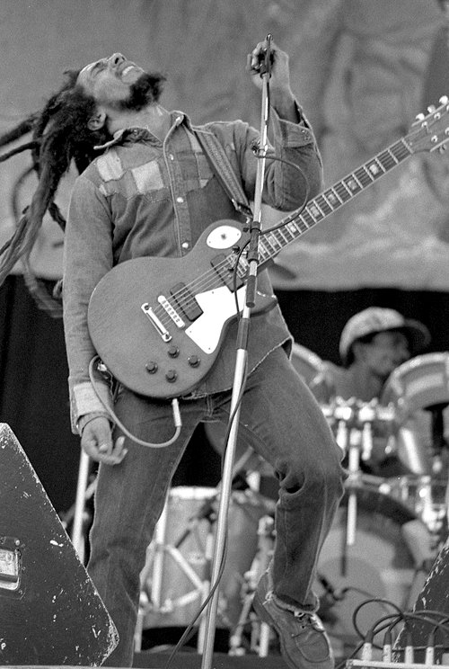 Bob Marley jouant de la guitare électrique sur scène lors d'un concert de reggae.