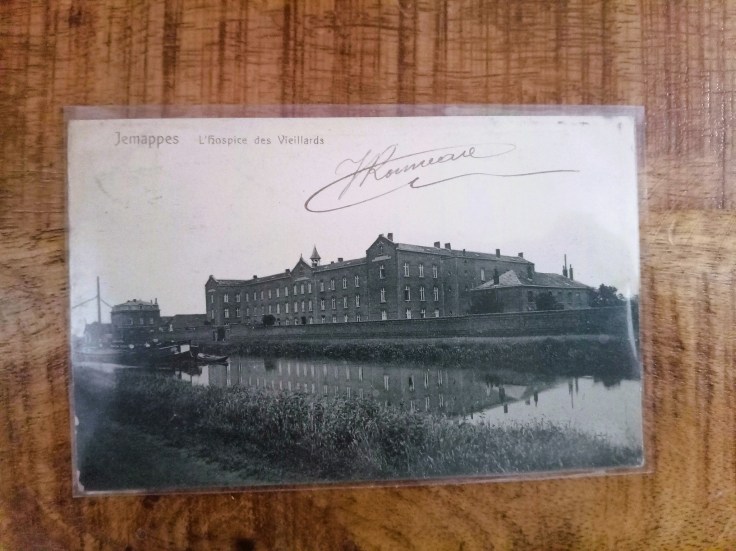 Carte postale ancienne en noir et blanc montrant le grand bâtiment de l'Hospice des Vieillards de Jemappes au bord d'un canal avec des reflets dans l'eau.